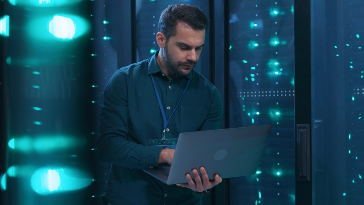 it professional admin using laptop computer doing data transfer operation with rack server cabinets